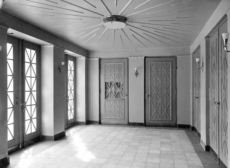 Helle Eingangshalle mit Glastüren, ornamentierten Türen und strahlenförmiger Deckenleuchte