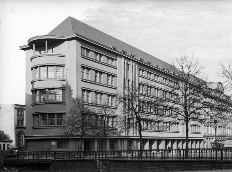 Mehrgeschossiger Putzbau mit gerundeter Ecke, Erkern und Walmdach, davor kahle Bäume