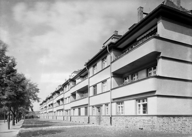 Dreigeschossiger Wohnblock mit gerundeten Balkonbändern und Flachdach, Rasenfläche und Baumreihe