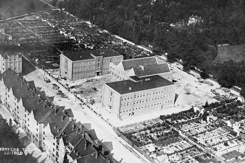 Luftbild: Schulanlage mit Klassenflügeln und Turnhallen inmitten von Wohnblöcken und Gärten