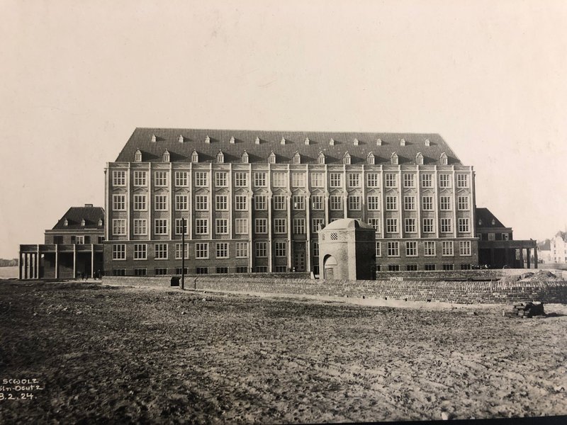Historisches Foto: großer mehrgeschossiger Schulbau mit Walmdach und Gauben, davor brachliegendes Gelände