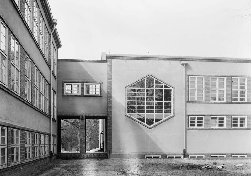 Schwarzweißfoto: Verbindungsbau mit großem sechseckigem Sprossenfenster neben mehrgeschossigem Schulflügel