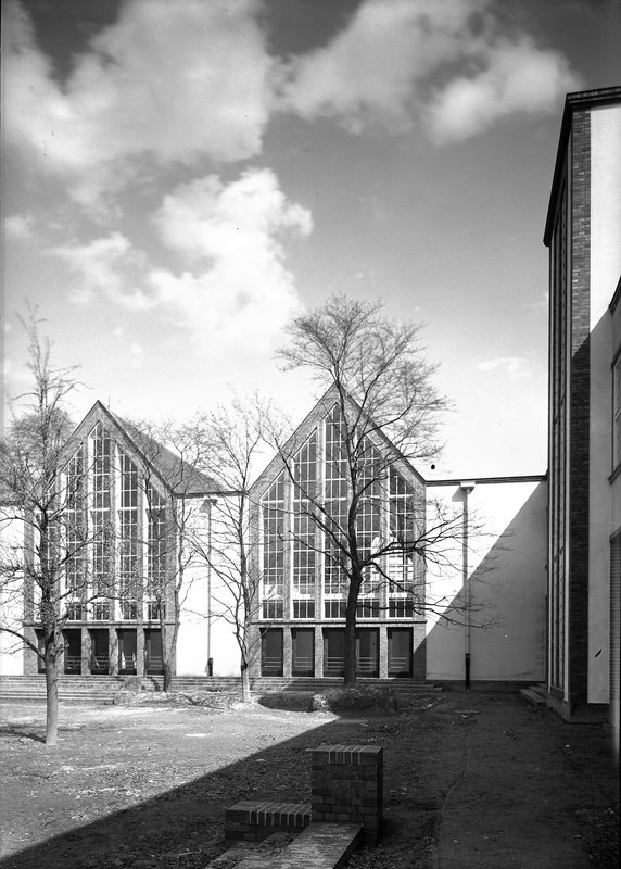 Schwarzweißfoto: zwei Turnhallen mit spitzen Giebeln und hohen Glasfronten, kahle Bäume im Hof