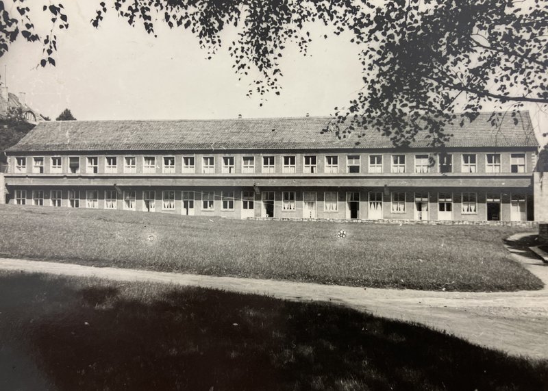 Langgestreckter zweigeschossiger Pavillonbau mit Fensterreihen hinter einer Wiese; Schwarz-Weiß-Fotografie